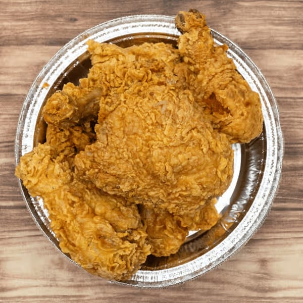 Golden brown fried chicken pieces in a silver foil takeout container on a wooden table.