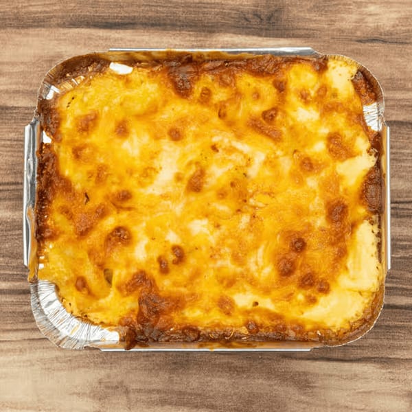 Baked Jamaican macaroni and cheese in a foil container on a wooden surface.