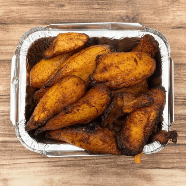 A foil container filled with golden-brown, fried Jamaican plantains on a wooden surface.