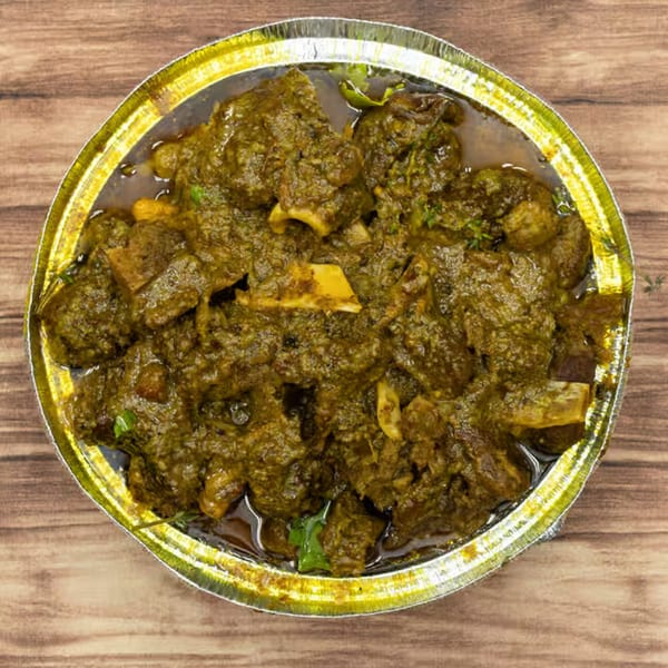 Close-up of Jamaican curry goat in a foil container on a wooden surface.