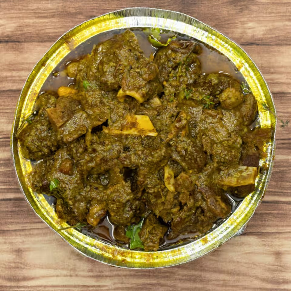 Close-up of Jamaican curry goat in a foil container on a wooden surface.