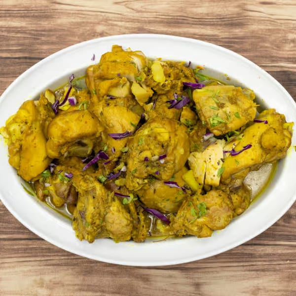 A white oval platter filled with Jamaican curry chicken, garnished with purple cabbage and green herbs.