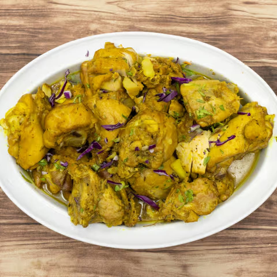 A white oval platter filled with Jamaican curry chicken, garnished with purple cabbage and green herbs.
